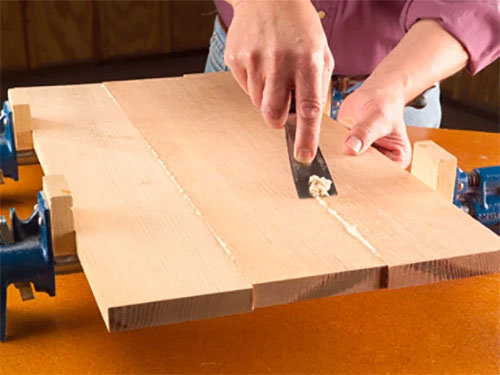  Using putty knife to scrap excess glue off panel