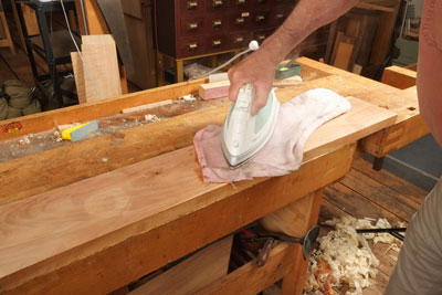 Using an iron to steam through a towel to repair dent in wood