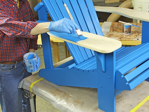 Applying blue paint onto an adirondack chair